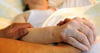  Ein Pfleger hält die Hand einer Frau. In Corona-Zeiten ist das Abschiednehmen in Heimen oder im Krankenhaus teilweise eingeschränkt.