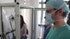 Dr. Dominik Buckert (re.) testet Katrin Egles Lungenfunktion. Dazu bläst sie in einem Glaskasten mehrere Male fest in eine Atemmaske.
