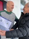 Vorsitzender Kurt Timm überreicht an der Haustür Reiner Peters seine Urkunde und Ehrennadel für eine 25-jährige Vereinstreue.
