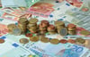 ARCHIV - ILLUSTRATION - Gestapelte Geldmünzen liegen am 04.11.2014 in München (Bayern) auf Geldscheinen. Am 03.02.2015 wird in Schwerin (Mecklenburg-Vorpommern) bei einer Kabinettssitzung unter anderem über die Verwendung des Haushaltsüberschusses vo