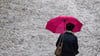 Ein Frau geht mit Regenschirm über eine Straße. Foto: Hendrik Schmidt/Archiv
