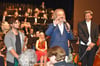  Worte des Lobes und der Anerkennung findet Komponist Alexander Krampe am Mikrofon für die Leistung von Emanuel Abanto an der E-Gitarre (links). Auch dem musikalischen Leiter der JPO, Alban Beikircher (rechts), ist nach diesem Auftritt sichtbar ein Stei