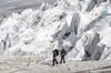 Schweiz, Rhonegletscher: Zwei Menschen wandern an dem mit Decken abgedeckten Rhonegletscher. Der älteste Gletscher der Alpen wird durch spezielle Decken vor dem Schmelzen geschützt. Die Gletscher in den Alpen sind vom Verschwinden bedroht. 