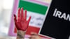 Eine rot bemalte Hand einer Frau erhebt sich zwischen Plakaten während einer Demonstration.