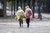 Menschen mit Plastik–Regenschutz gehen durch den Regen.