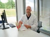 Chefarzt Dr. Andreas Junghanns demonstriert am Schreibtisch die verschiedenen Behandlungsmöglichkeiten der Arthrose an den Fingergelenken. In der Hand hält er eine Prothese für das Fingermittelgelenk.
