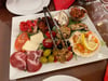 Reichhaltige Antipasti: Köstlichkeiten wie Parmigiana, Bruschetta, gratinierte Muscheln und gefüllte Riesenchampignons auf einem Teller.