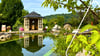 Ansicht eines Naturpool mit Blick auf das Wasser, das Poolhaus und eine Entspannungsliege im Garten